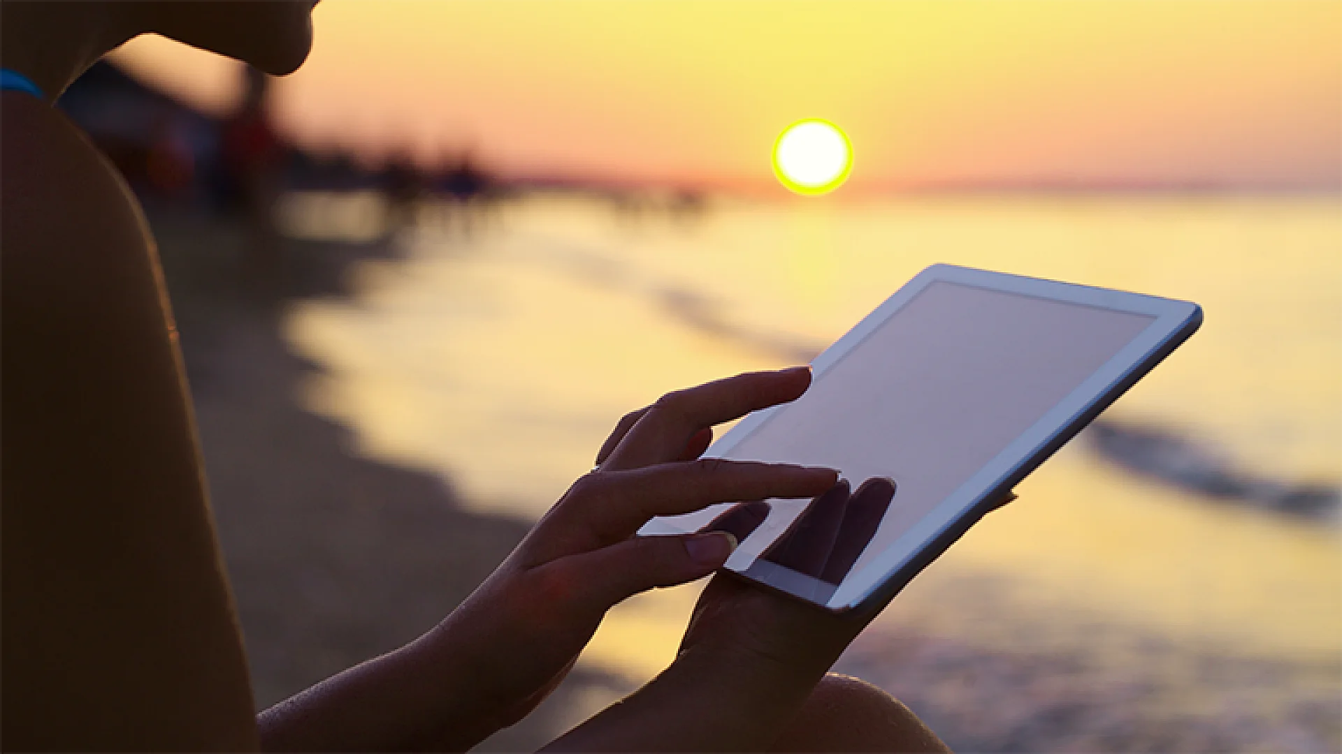 Person bedient Tablet am Strand bei Sonnenuntergang