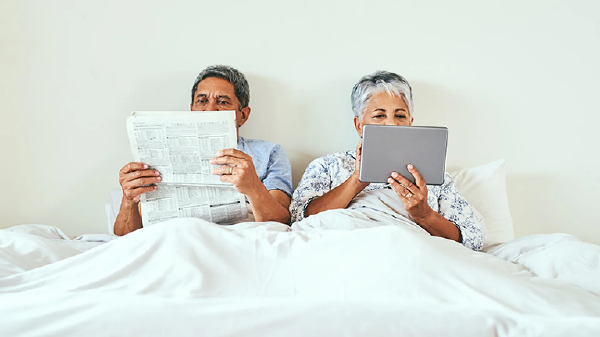 Paar genießt gedruckte und digitale Zeitung im Bett, zeigt gemütliches Lesen beider Formate